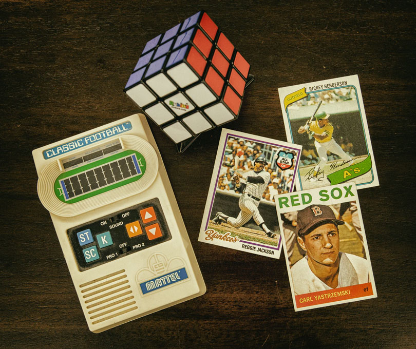 80s memorabilia baseball cards, classic football game, and rubik’s cube on brown table