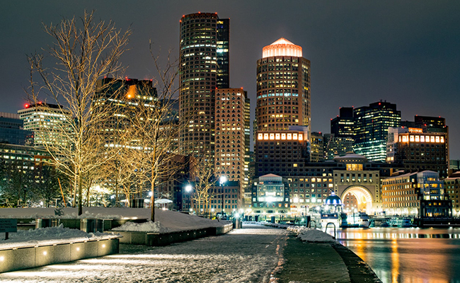 A lit-up Boston, Massachusettes skyline in the snow.