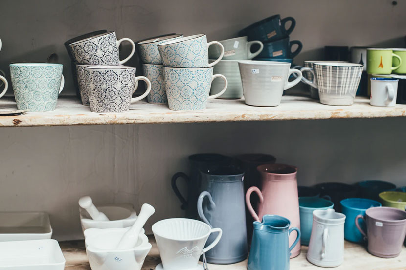 A collection of cups, mugs, and other vessels sit for sale on a set of shelves
