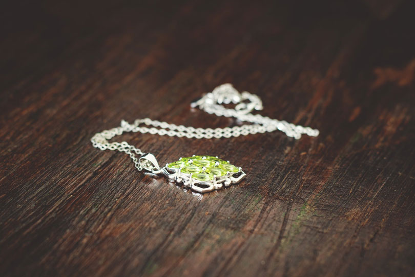 A silver necklace with green stone pendant rests on a wooden surface
