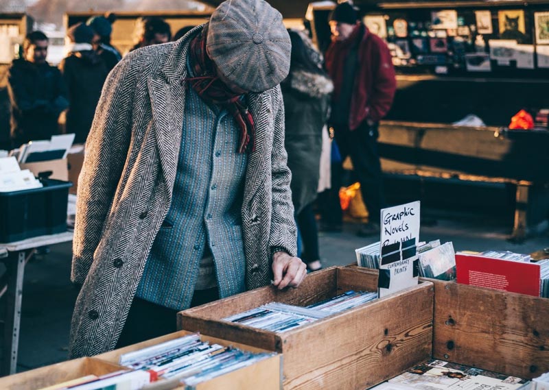 man looking at a box of books for sale on a table