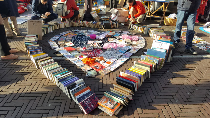 people looking at books displayed in the shape of a heart on a brick road