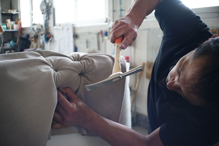 A man works on a piece of reused furniture upholstery with a tack hammer